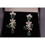 A pair of white metal drop earrings set with emeralds and single cut diamonds.