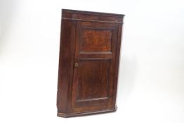 A 19th century oak corner cupboard with panelled door enclosing two shelves,