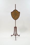 An Edwardian mahogany shield shape fire screen with needlepoint floral panel and height adjustable