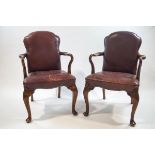 A pair of Maple and Co elbow chairs in the George II style, with leather shaped backs and seats,