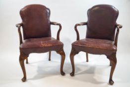 A pair of Maple and Co elbow chairs in the George II style, with leather shaped backs and seats,
