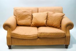 An early 20th century two seater sofa on turned wooden legs, salmon pink upholstery,