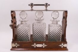 A mid-20th century oak tantalus with plated mounts, three pressed glass bottles and stoppers,