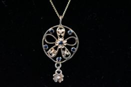 A yellow metal floral pendant set with sapphires and suspended from a curb link chain.