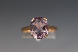 A yellow metal single stone ring set with an oval amethyst.