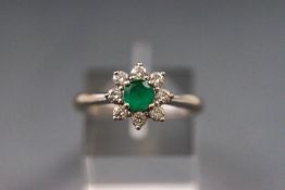 A white metal cluster ring set with emerald and diamonds. Hallmarked 18ct gold, Sheffield.
