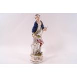 A Meissen figure of a man in a blue jacket holding a bird,