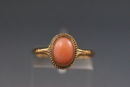 A yellow metal single stone ring set with a cabochon coral.