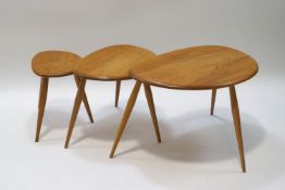 An Ercol blond wood pebble nest of three tables, the largest with label,