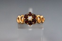 A yellow metal cluster ring set with a opal and surrounded by garnets.