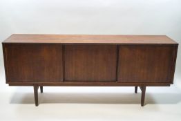 A mid 20th century sideboard with sliding doors enclosing three drawers,