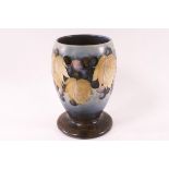 A Moorcroft pottery salt glaze footed vase, decorated wtih grapes on a blue ground, factory marks,