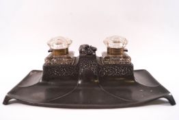 An Art Nouveau pewter deskstand with two cut glass inkwells to either side of a compartment,