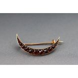 A yellow metal crescent brooch set with graduated garnets. Pin and hook fitting.