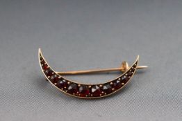 A yellow metal crescent brooch set with graduated garnets. Pin and hook fitting.