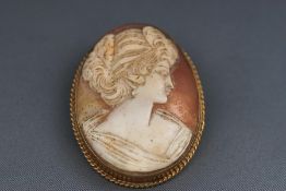 A yellow metal carved cameo brooch with rope edge design.