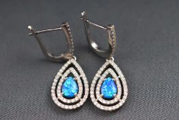A modern white metal pair of drop earrings set with blue synthetic opal and cubic zirconia.
