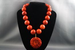 A carved coral pendant suspended from circular coral beads and silver T bar clasp.