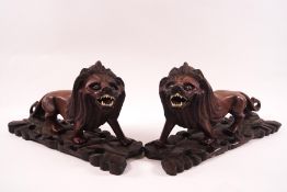 A pair of Chinese carved hardwood lions with glass eyes and bone teeth, 26cm long,