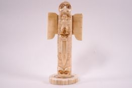 A bone carving of a totem pole, decorated with animal and human spirits in relief,