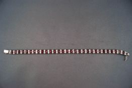 A white metal line bracelet set with red and white paste stones.