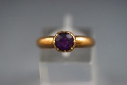 A yellow metal single stone ring set with a round faceted amethyst. Tests indicate 18ct gold.