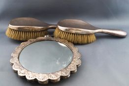 An Indian round mirror in lobed white metal frame, embossed with repeating designs of flower heads,