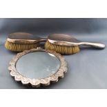 An Indian round mirror in lobed white metal frame, embossed with repeating designs of flower heads,