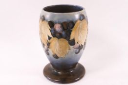 A Moorcroft pottery salt glaze footed vase, decorated with grapes on a blue ground, factory marks,