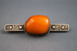 A white metal bar brooch set with a butterscotch amber. Tests indicate sterling silver.
