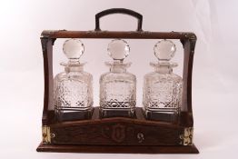 An early 20th century oak and cut glass three bottle tantalus, with plated mounts (no maker's name),