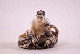 An early 20th century Japanese ivory netsuke, carved as a seated man holding a rope,