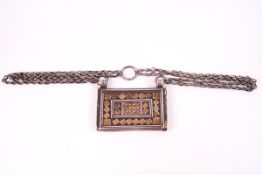 An Oman white metal Koran holder with geometric pattern in relief, on a chain, 7.3cm x 5.5.