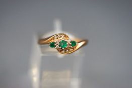A yellow gold crossover dress ring set with emeralds and diamonds.