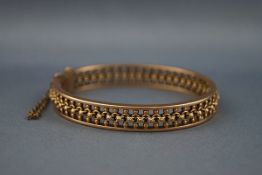 A yellow gold bangle having a pierced beaded filigree design with hinge fitting and push in clasp.