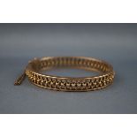 A yellow gold bangle having a pierced beaded filigree design with hinge fitting and push in clasp.