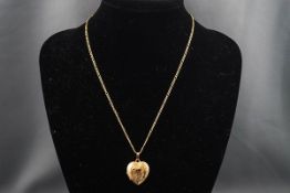 A yellow gold engraved heart locket suspended from a hollow yellow gold figaro chain.