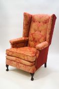 A George III style button back wing armchair with carved oak claw and ball feet,