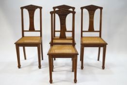 A set of four Arts & Crafts oak dining chairs with carved vine detail to the backs and cane seats