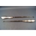 Two large silver handled button hooks, each with a shaped wavy handle,