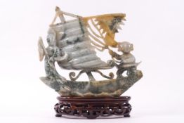 A Chinese jadeite carving of two figures on a ship, upon a carved wood stand,