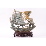 A Chinese jadeite carving of two figures on a ship, upon a carved wood stand,