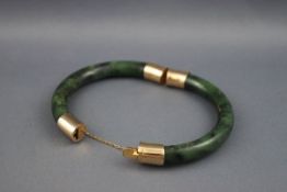 An Oriental green and black mottled hardstone hinged-bangle imitating jade with yellow metal mounts