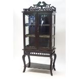 A Victorian ebonised display cabinet, the glazed doors enclosing three shelves,