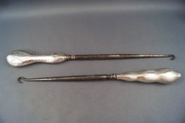 Two large silver handled button hooks, each with a shaped wavy handle,