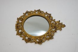 A circular wall mirror with scrolling feathered metal frame, painted cream and gilt,