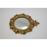 A circular wall mirror with scrolling feathered metal frame, painted cream and gilt,