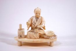 An early 20th century Japanese ivory okimono of a seated man with tablewares,