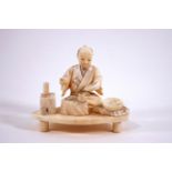 An early 20th century Japanese ivory okimono of a seated man with tablewares,