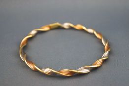A 9ct tri coloured gold twisted gold bangle, 7cm diameter, applied pad marked "9KT" "Italy",